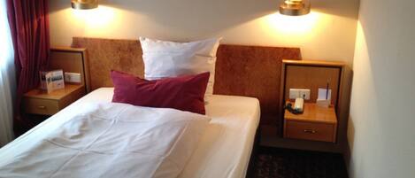 Una habitación de hotel con una cama grande, dos mesitas de noche y un cabecero.