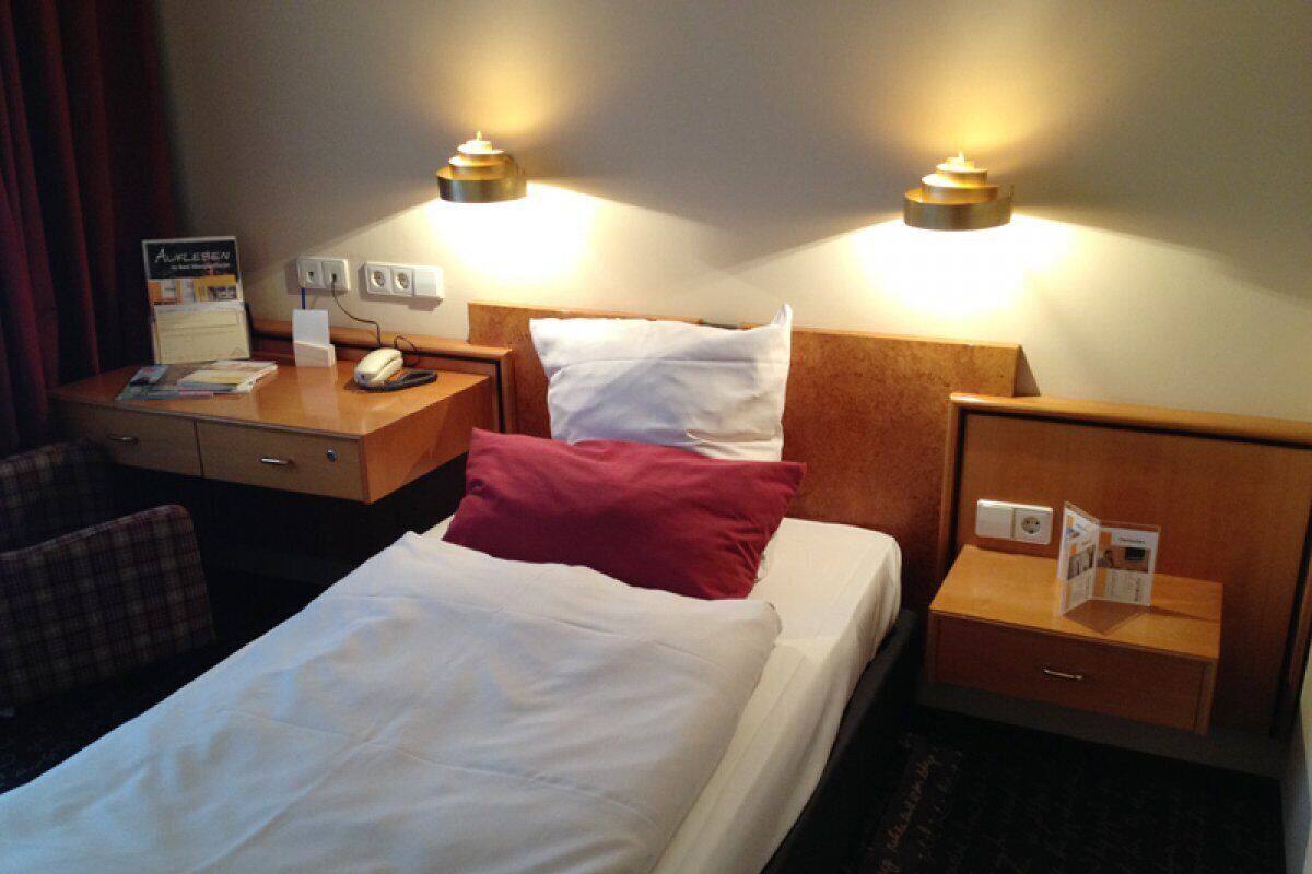 Una habitación de hotel con una cama bien hecha, un escritorio con un teléfono y una revista, y dos lámparas de noche.