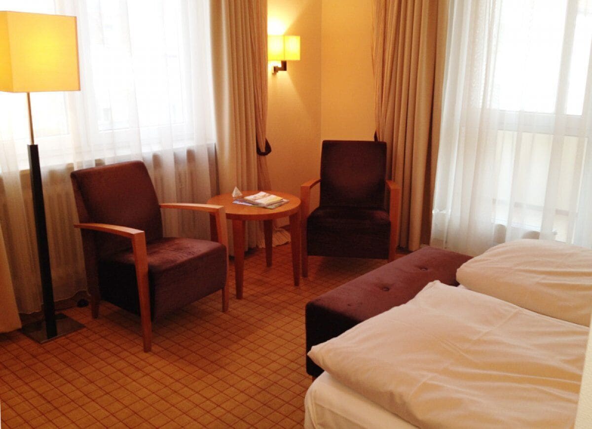 A hotel room with a bed, two armchairs, a small table, and a lamp.