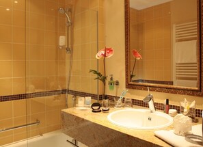 Un baño con cabina de ducha de vidrio, un lavabo con encimera de mármol y un espejo grande con marco decorativo.