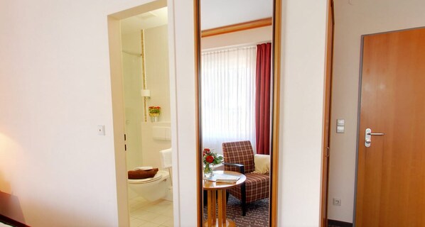 Una habitación de hotel con baño, una zona de comedor con mesa y silla, y una puerta de madera.