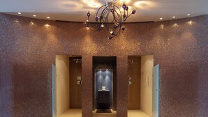 Un baño moderno con paredes de mosaicos, un lavabo central y una araña.