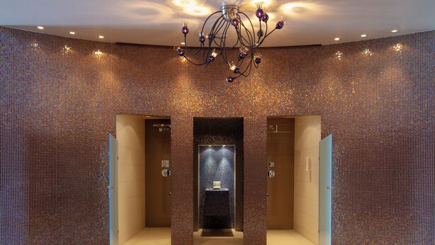 A modern bathroom with mosaic tile walls, a central sink, and a chandelier. - Ringhotel Bundschu (Bad Mergentheim)