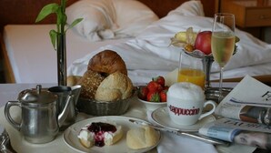 A breakfast setup with croissants, a cappuccino, fruit, and a glass of orange juice on a table in a hotel room. - Ringhotel Bundschu (Bad Mergentheim)