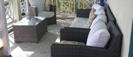 A covered outdoor seating area with wicker furniture and a concrete floor.