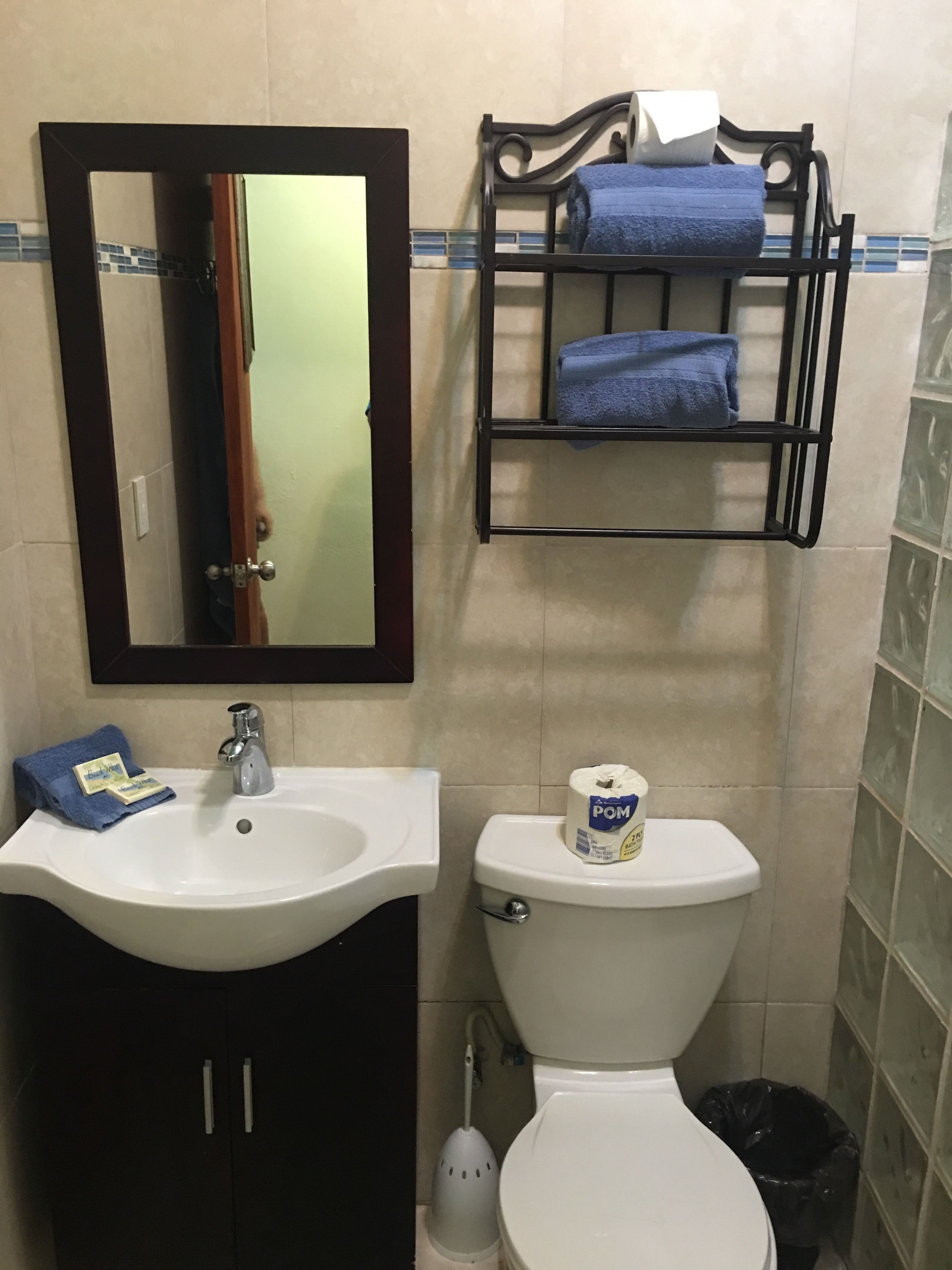 Un baño con un lavabo blanco, un espejo, un inodoro, un perchero con toallas y un cubo de basura.