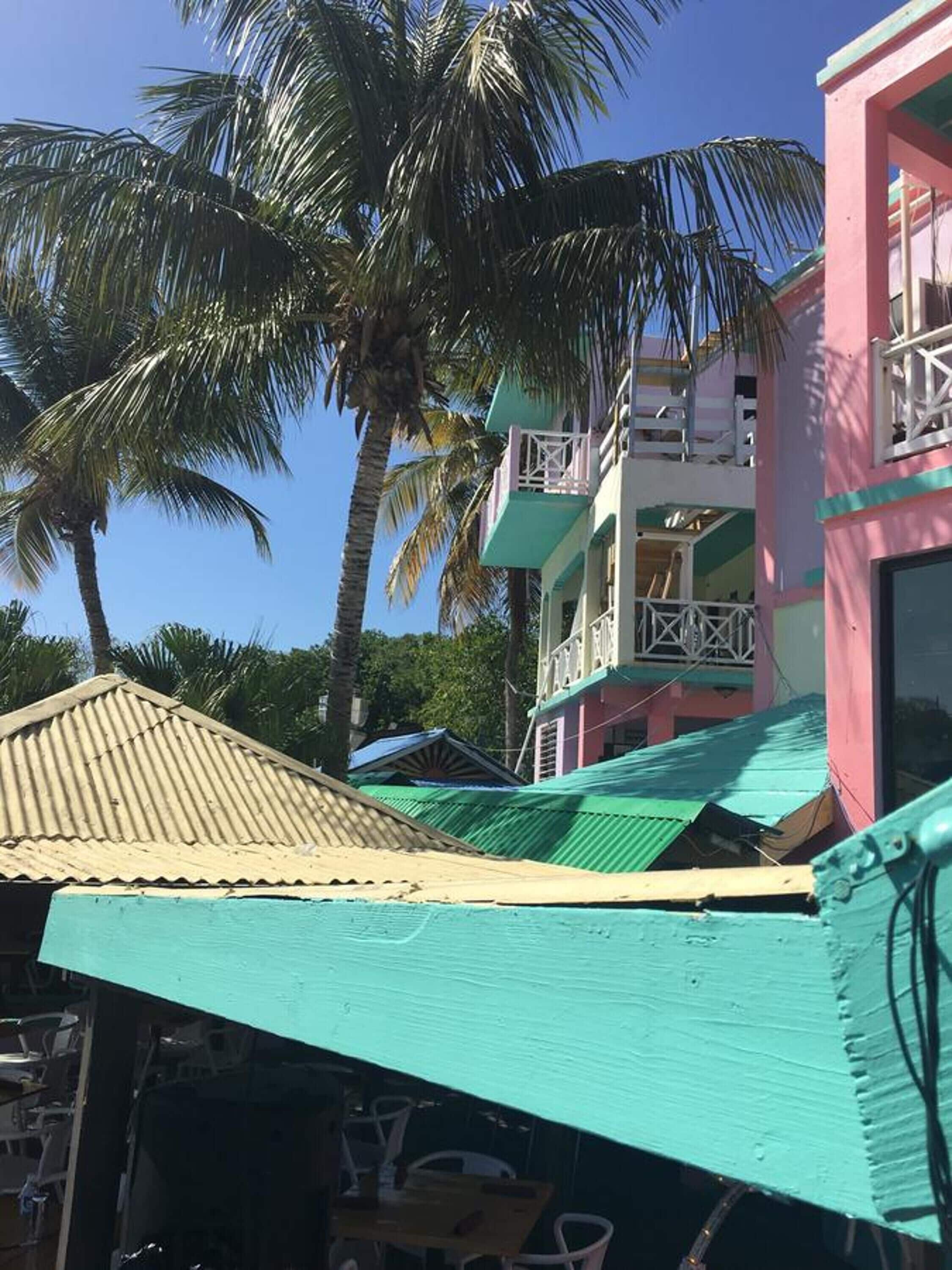 Un edificio con techo verde, fachada rosa y un balcón con barandilla blanca.
