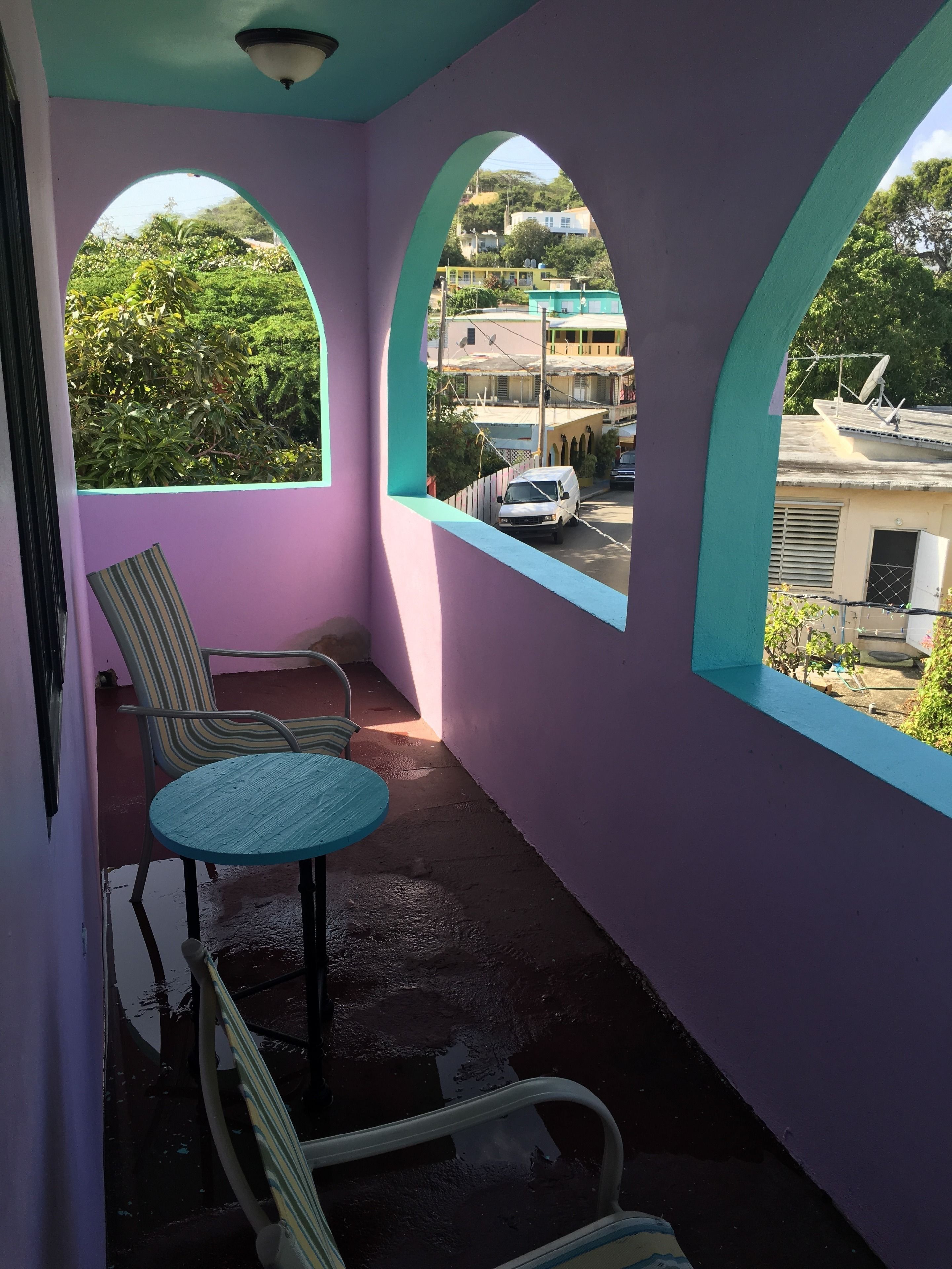 A balcony with a purple wall, two arched windows, a striped chair, and a small table.