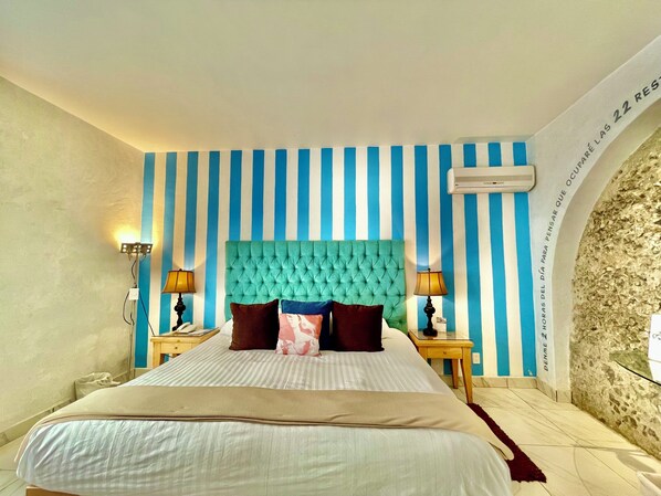 Habitación de hotel con una cama grande, paredes a rayas y un muro de piedra decorativo.