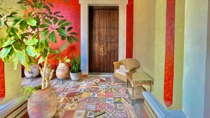 A hallway with a red wall, a wooden door, and a patterned floor. There are potted plants and a wicker chair. - El Sueño Hotel & Spa (Puebla)