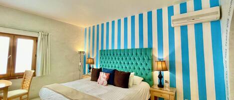 Habitación de hotel con una cama grande, dos mesitas de noche, un ventanal con cortinas y una pared a rayas.
