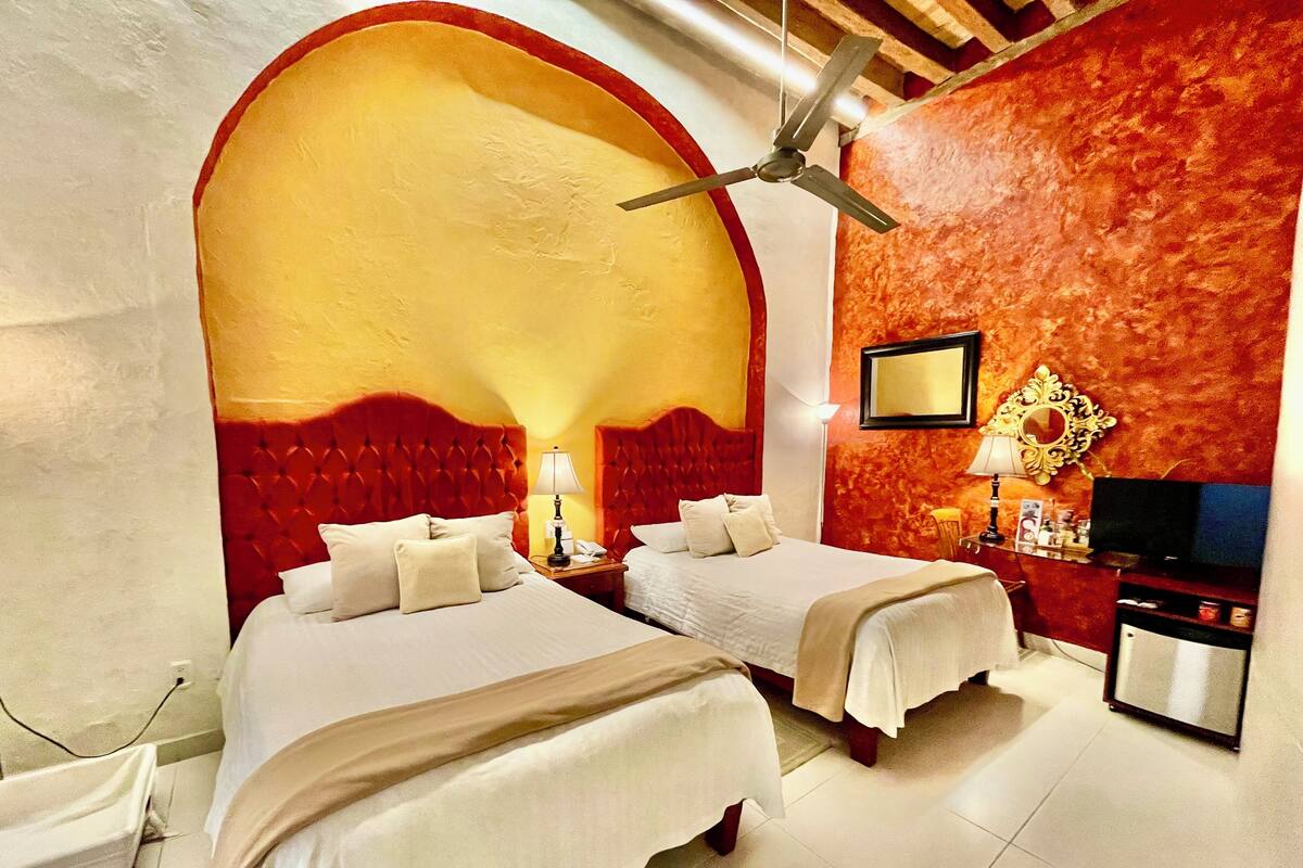 A hotel room with two beds, a red accent wall, a ceiling fan, and a television.