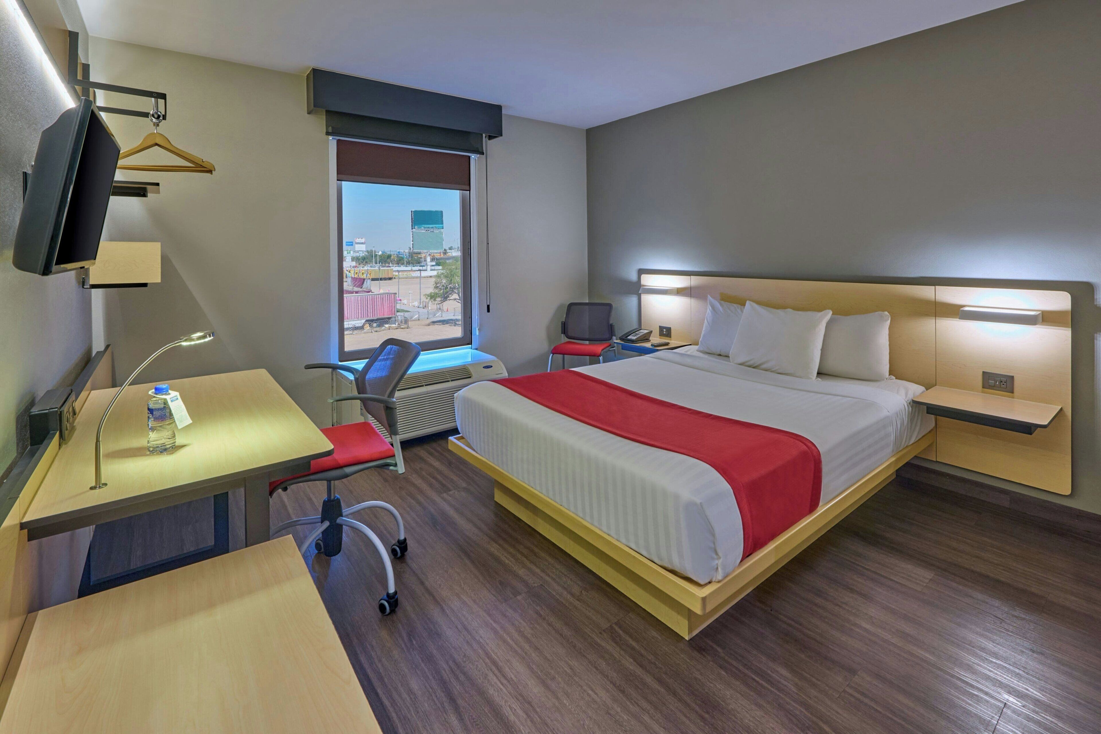 A hotel room with a bed, desk, chair, TV, and a window with a view.