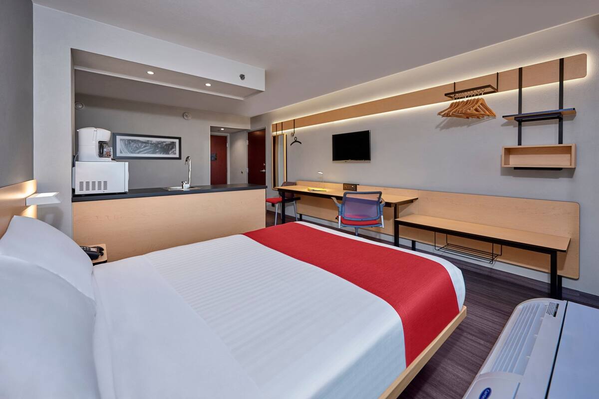 A hotel room with a large bed, a desk with a chair, a television, and a coffee machine.