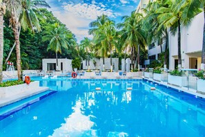 A swimming pool with lounge chairs and palm trees, surrounded by a white building with multiple floors. - Smart Cancun The Urban Oasis (Cancun)