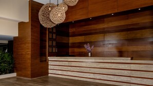 A reception area with a wooden reception desk, wicker pendant lighting, and a vase with flowers. - Smart Cancun The Urban Oasis (Cancun)