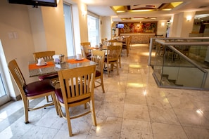 A hotel dining area with multiple tables and chairs, a television screen, and a kitchen counter in the background. - Hotel Plaza Calzada (Monterrey)