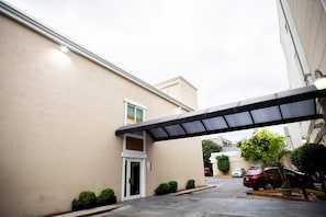 A building with a covered entrance, a parking area, and a few cars parked outside. - Hotel Plaza Calzada (Monterrey)