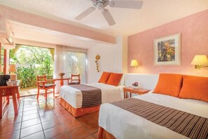 Habitación de hotel con dos camas, un ventilador de techo, una mesita con lámpara y vistas a zonas verdes.