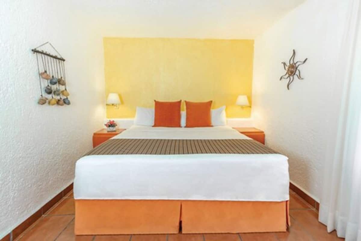 A hotel room with a large bed, two bedside tables with lamps, a wall-mounted decorative item, and a small plant on one table.