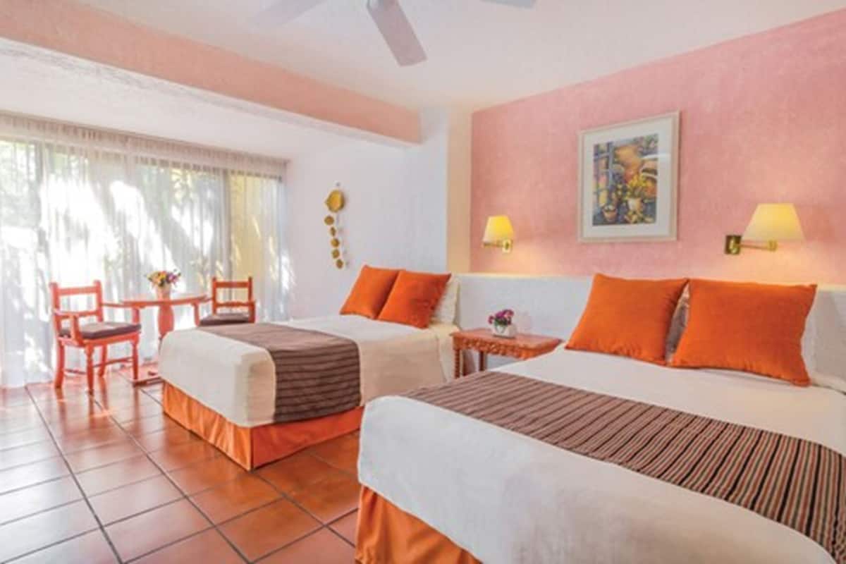 A hotel room with two beds, a small table, chairs, and a window with curtains.