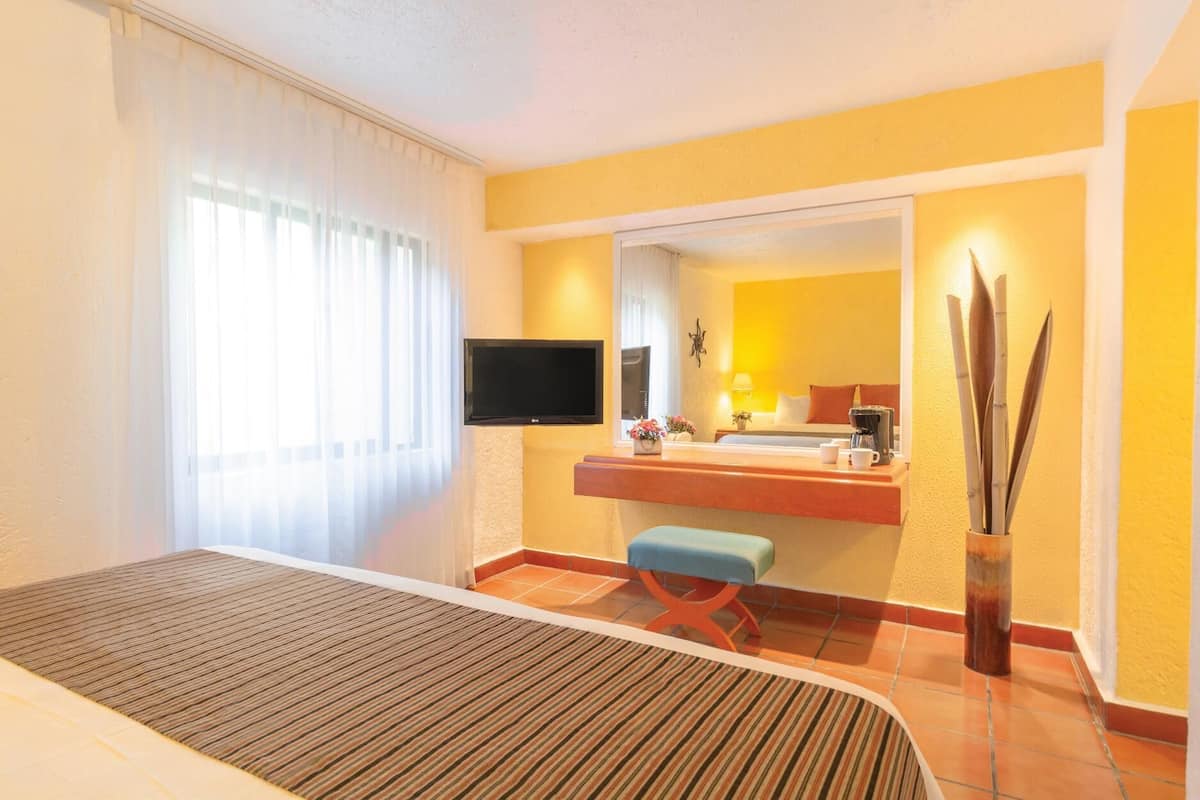 A hotel room with a bed, a television, a bathroom with a mirror, and a small table with a coffee maker.