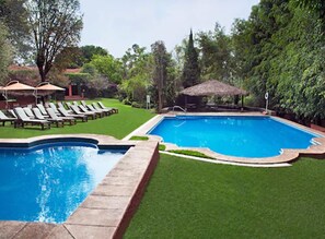 Una piscina con una estructura de techo de paja, rodeada de un césped cuidado y sillas de descanso.