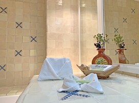Um banheiro com paredes revestidas de azulejos bege, uma toalha branca no chão e dois vasos com flores.