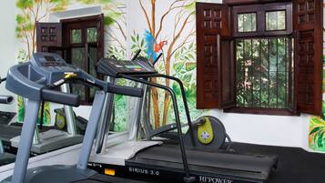 A treadmill with a digital display, positioned in a room with a mural of trees and windows with wooden shutters.