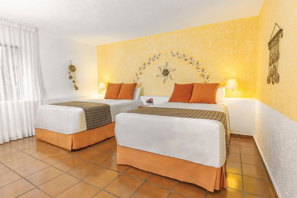 A hotel room with two beds, a sun decoration on the wall, and a lamp on each side.