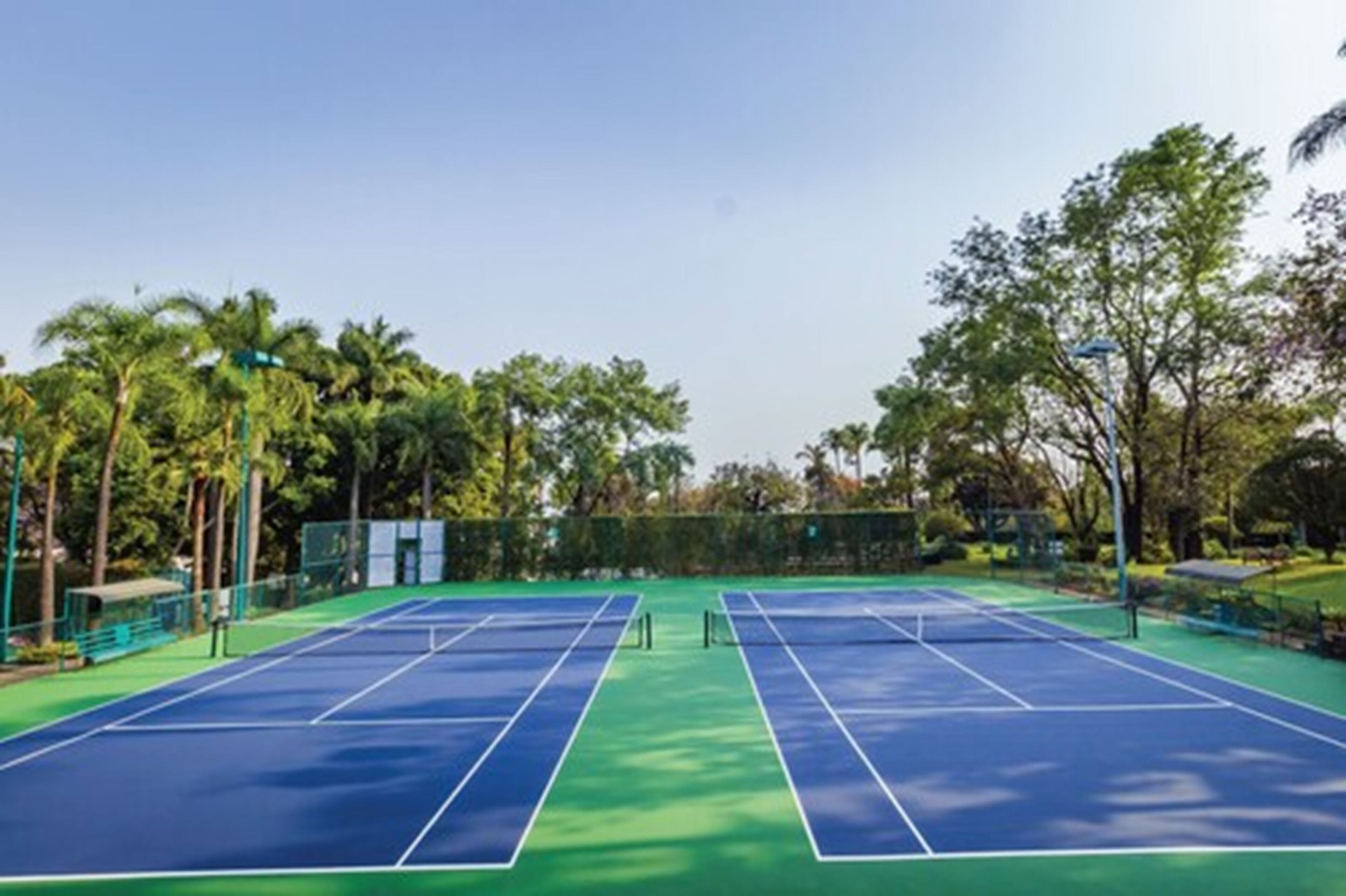 An outdoor tennis court with a green and blue surface, surrounded by trees and a fence.
