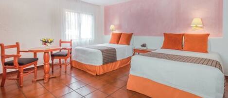 A hotel room with two beds, a dining table with chairs, and a ceiling fan.