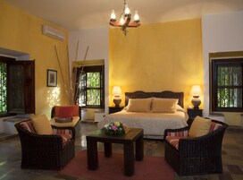 Una habitación con una cama, dos sillones de mimbre, una mesita con un jarrón de flores y dos lámparas de noche.