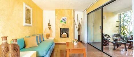 Una sala de estar con sofá, una mesa de centro y chimenea. Hay una puerta corrediza de vidrio que da a un área exterior con sillas.