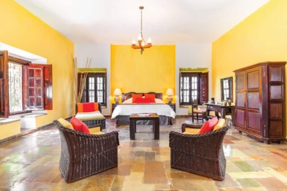 A hotel room with a bed, two wicker chairs, a small table, and a chandelier.