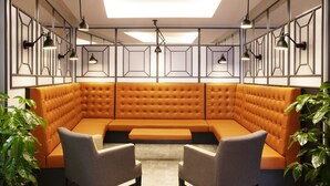 A modern lounge area with a large orange sectional sofa, two grey armchairs, and pendant lighting. - Fosshotel Barón (Reykjavik)