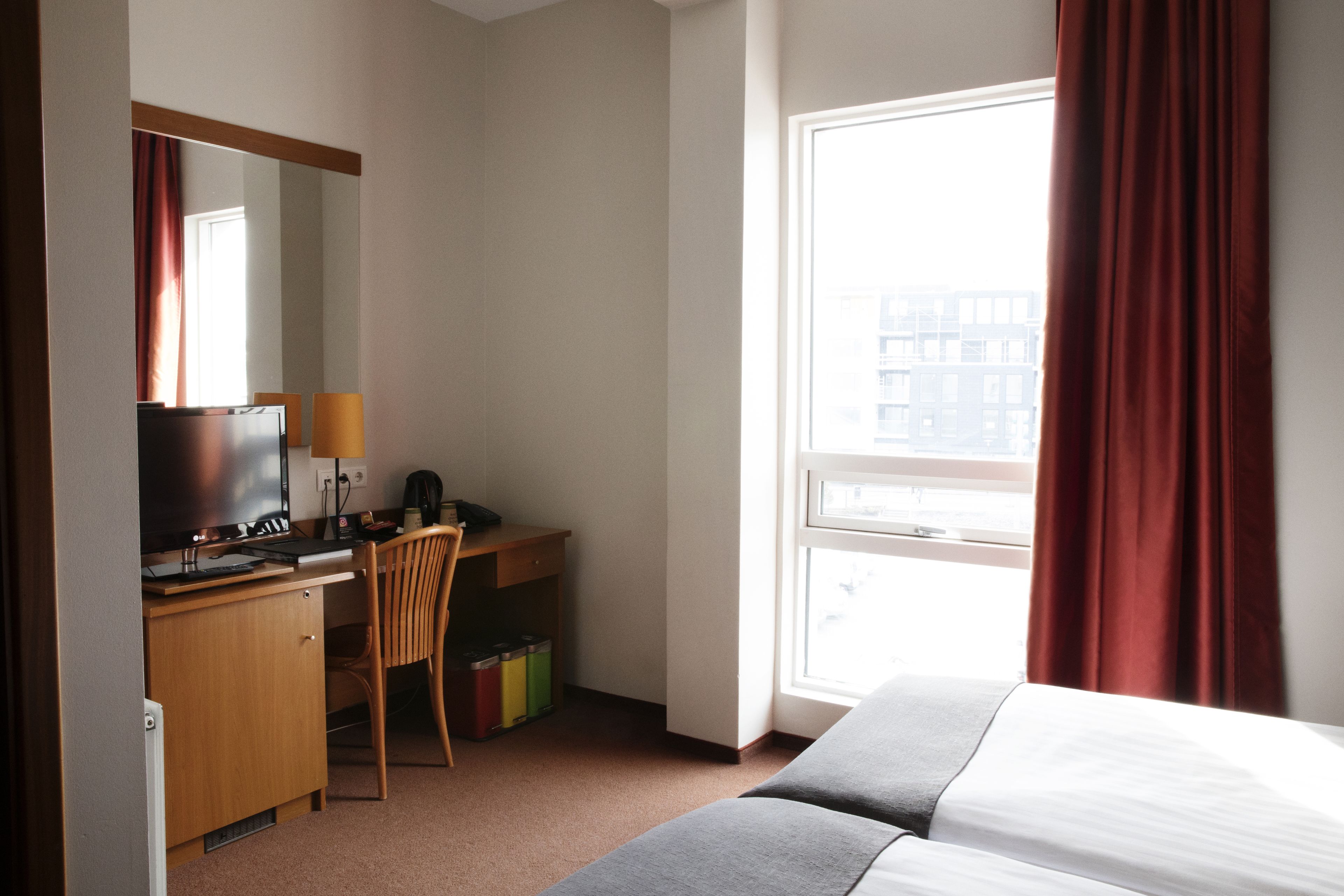 Une chambre d’hôtel avec un lit, un bureau avec un ordinateur, une chaise, une télévision et une fenêtre avec des rideaux.