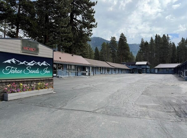 A large, empty parking lot with a sign for Tahoe Sands Inn, surrounded by trees and mountains.