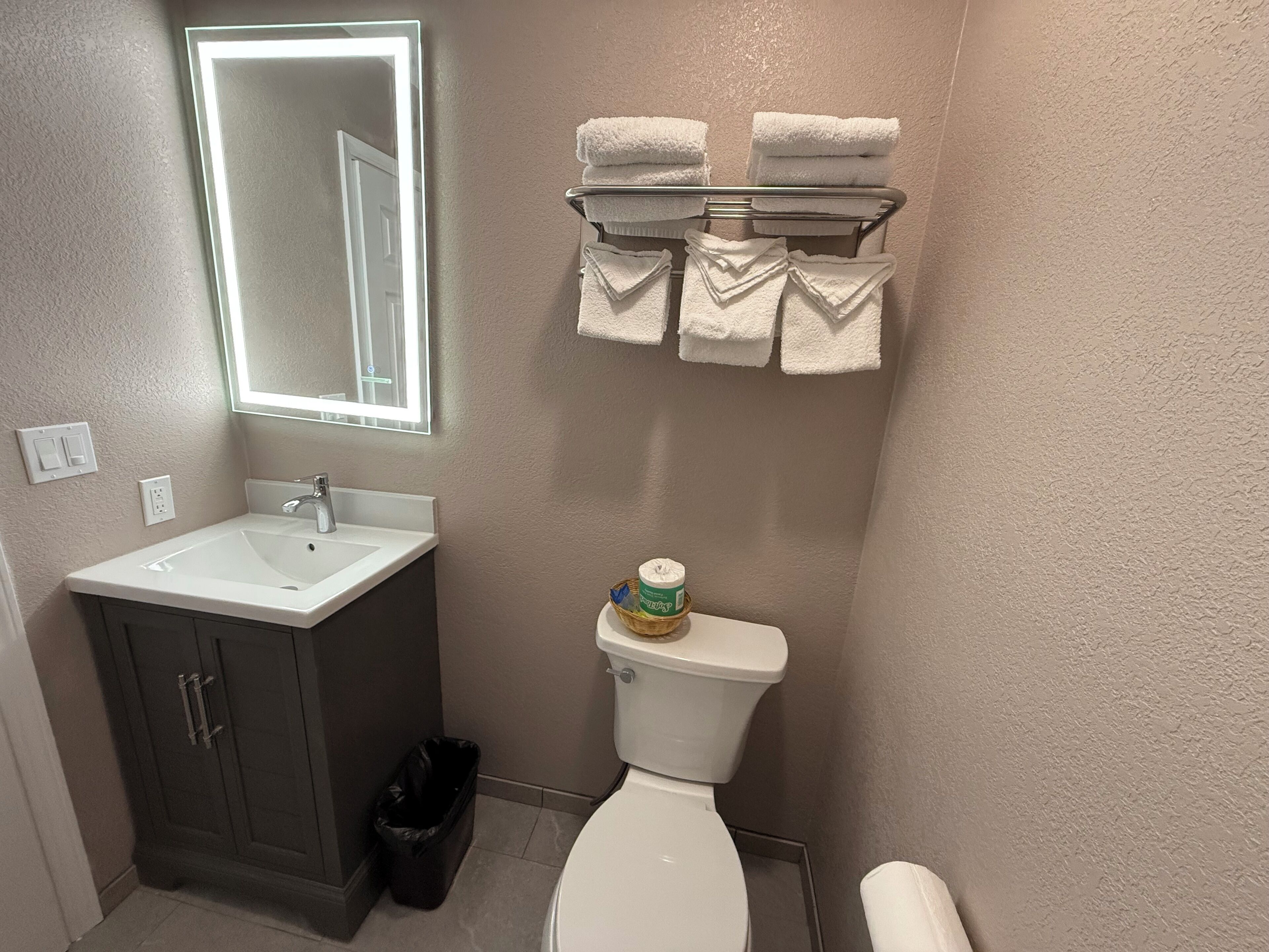 A bathroom with a white sink, a mirror, a toilet, and a towel rack with folded towels.
