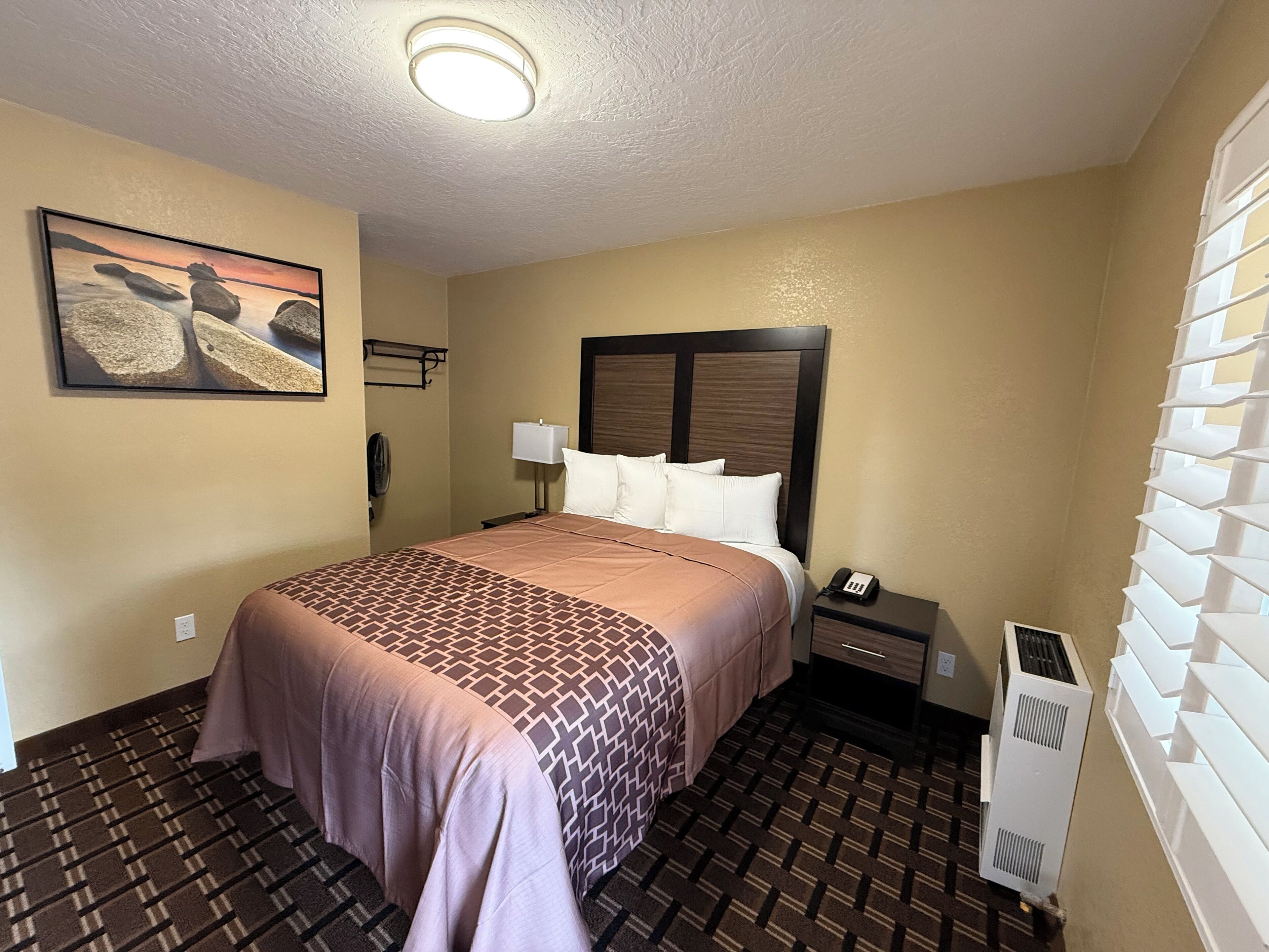 Ein Hotelzimmer mit Bett, Nachttisch, Lampe, Telefon und Heizung.