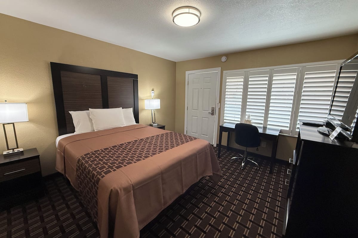A hotel room with a bed, bedside tables, a desk, and a chair.