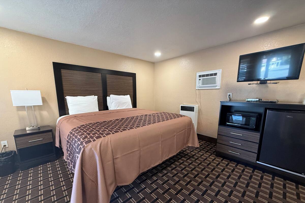 A hotel room with a bed, a TV, a desk, a microwave, and an air conditioning unit.