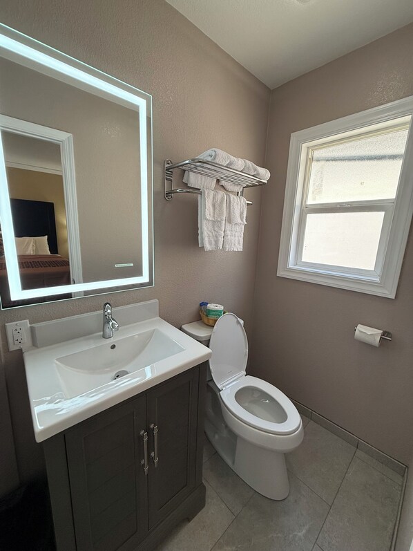 Une salle de bain équipée d’un lavabo, d’un miroir, de toilettes, d’un porte-serviettes et d’une fenêtre.