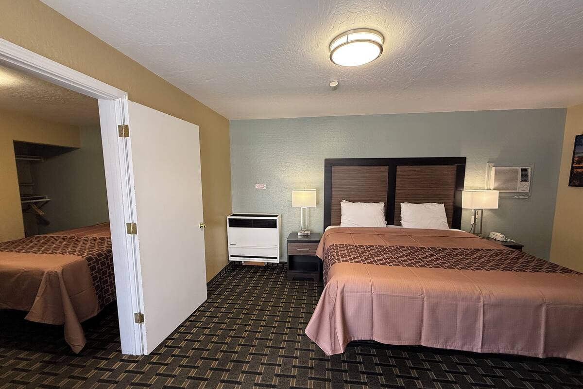 A hotel room with two beds, a wardrobe, a bedside table with a lamp, an air conditioning unit, and a ceiling light.