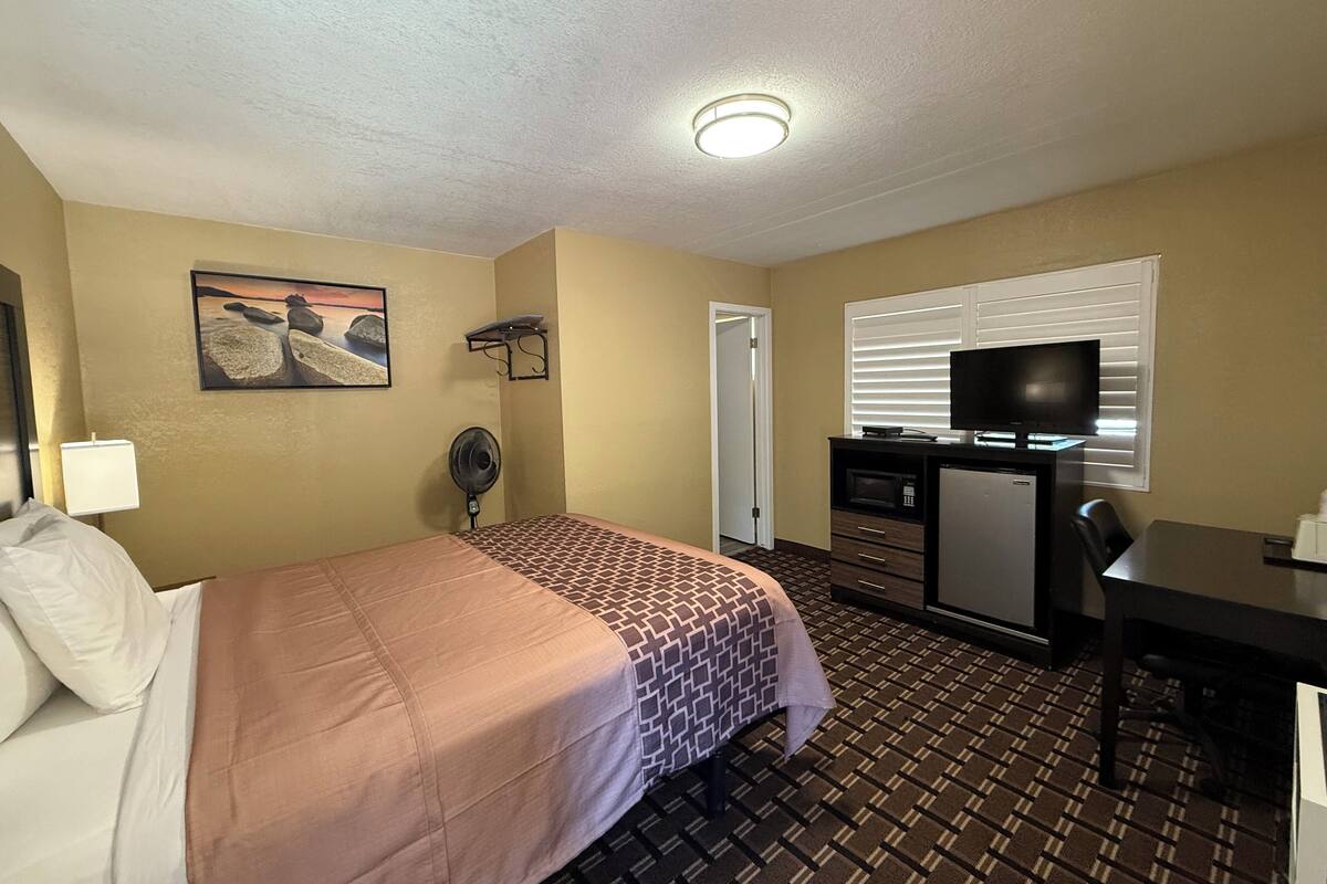 A hotel room with a bed, a desk, a TV, a microwave, and a fan.
