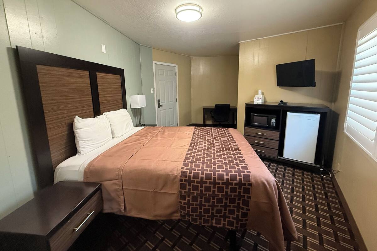 A hotel room with a bed, a desk, a television, and a door.