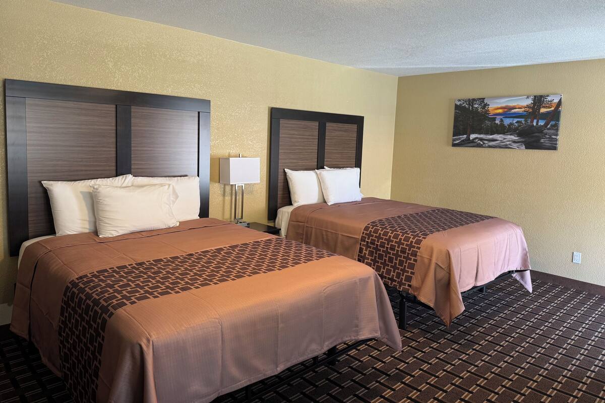 A hotel room with two beds, a nightstand, a lamp, and a painting on the wall.