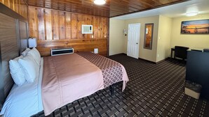 Une chambre d’hôtel avec un plafond en bois, un lit recouvert d’une couvre-lit à motifs, un bureau avec une chaise, un tableau au mur et une porte.