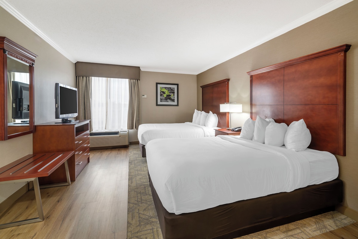 A hotel room with two beds, a desk, a TV, and a window with curtains.