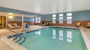 Une piscine intérieure à l’eau d’un bleu limpide, entourée de murs recouverts de carreaux beiges et bruns, et dotée de chaises longues et d’un espace vestiaire.